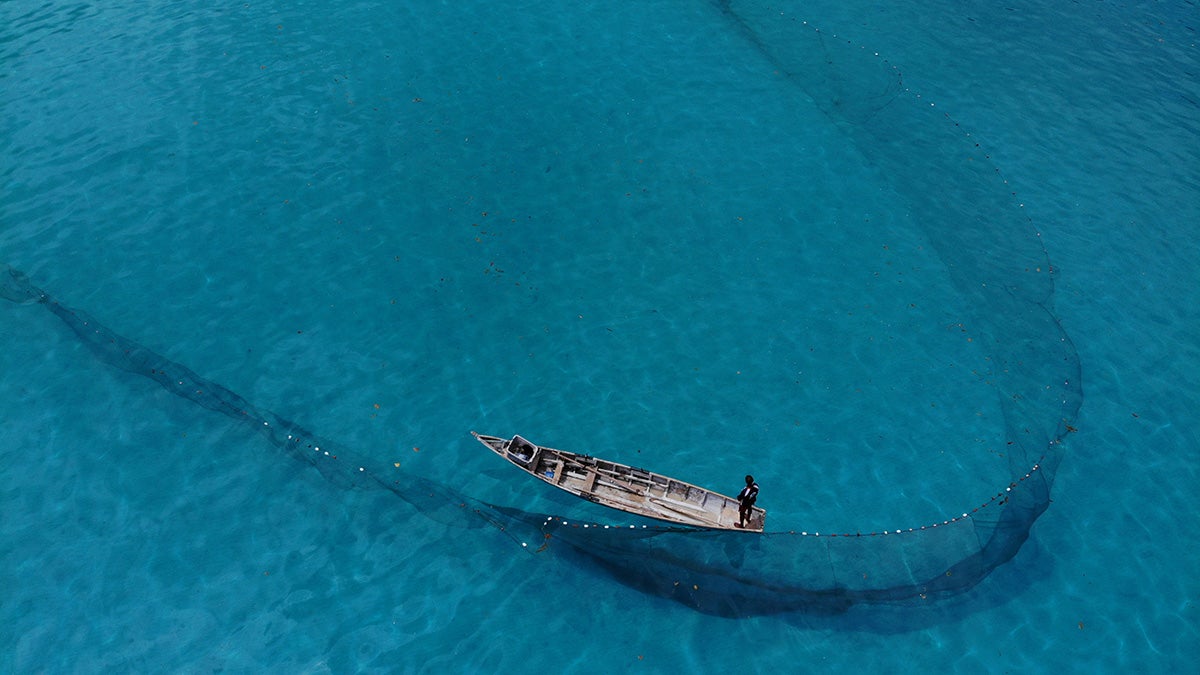 Fisherman on boat with nets in clear blue water