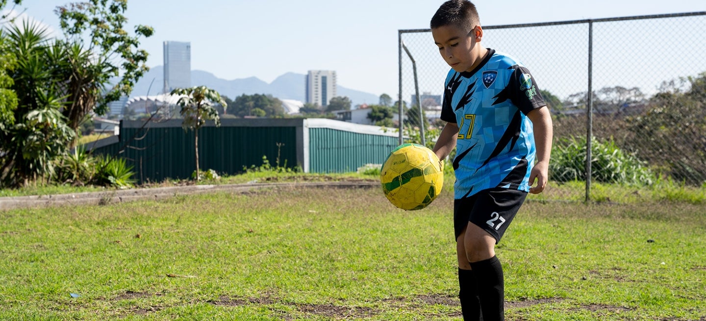 Boy kicking soccer ball in a field, Alajuelita, Costa Rica