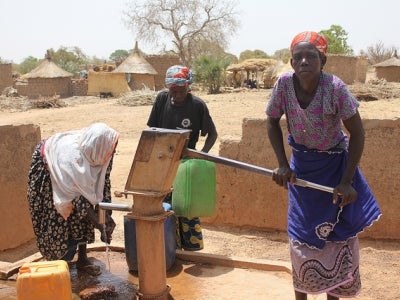 Women using a water pump in an arid landscape