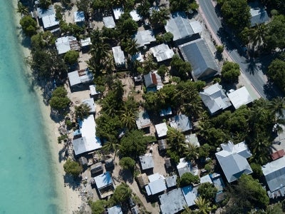 Aerial view of tropical island Kiribati coastline, with houses, trees, and a boat in the ocean