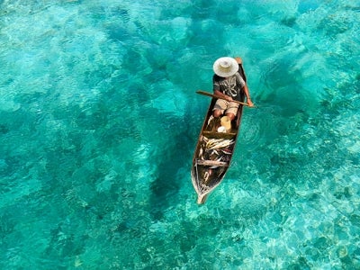 Fisherman in boat surrounded by clear, turquoise waters