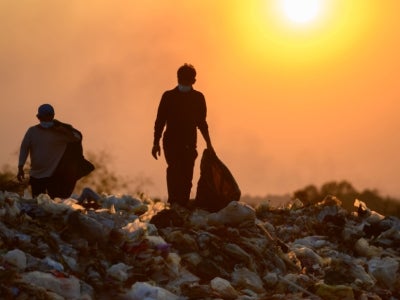 People at a landfill collecting trash with a bright sun in background