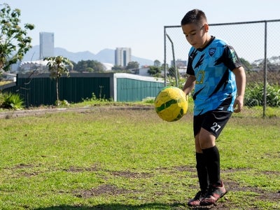 Boy kicking soccer ball in a field, Alajuelita, Costa Rica
