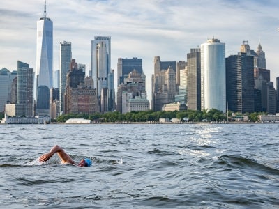 Man swimming in river with New York City skyline in background