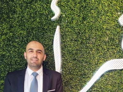 Man standing in front of a grassy wall with Arabic lettering