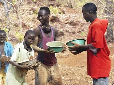 Children pan for gold against an arid backdrop in Burkina Faso.