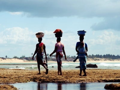 Mozambique women carrying basket on the head and baby behind the back walking home after looked for mussels at Tofo beach, Mozambique. Photo: Aostojska/Shutterstock.
