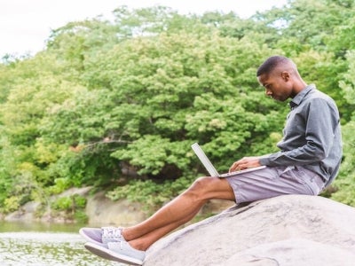 Young man on sitting in Central Park while working on his computer.
