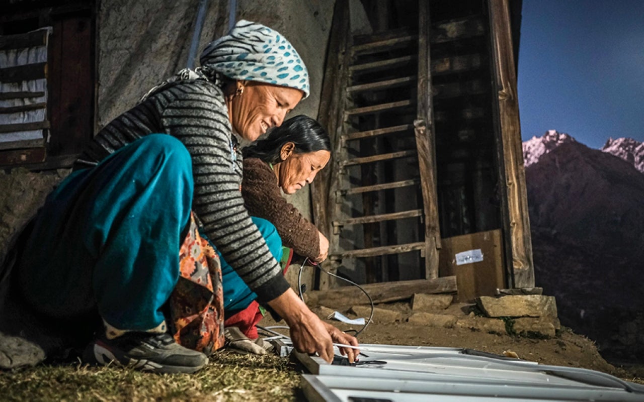 Two women working on a solar panel with mountain in background