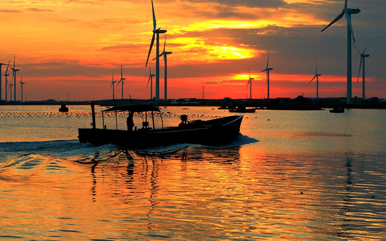 Boat traveling through an aquaculture area of the Yellow Sea. Windmills in background with colorful sunset
