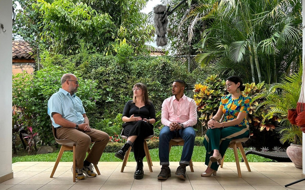 Four people sitting having a discussion with a green plant background