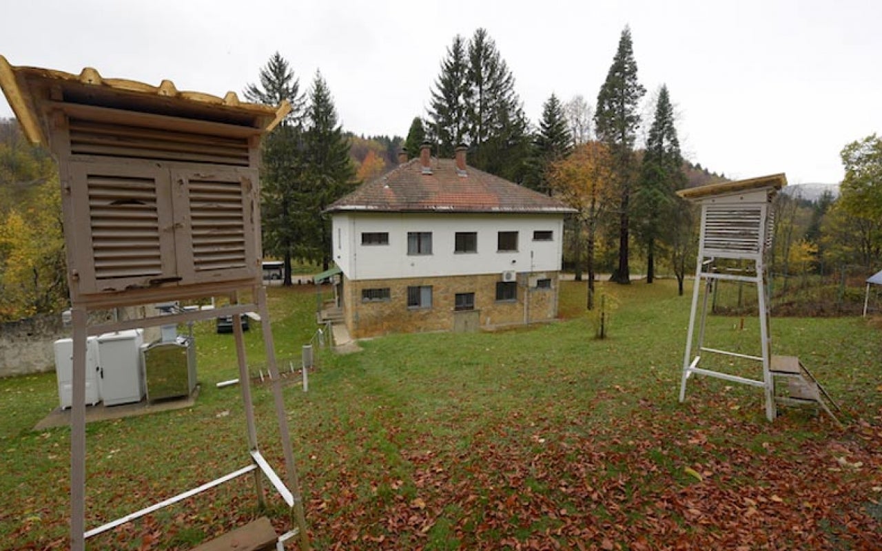 House in forested valley with two air quality monitoring stations in foreground