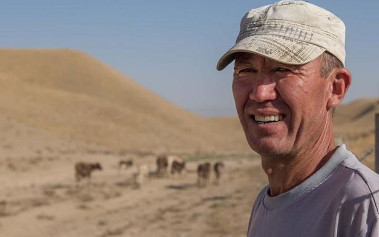 Farmer standing alongside herd in arid, mountainous area of Tajikistan