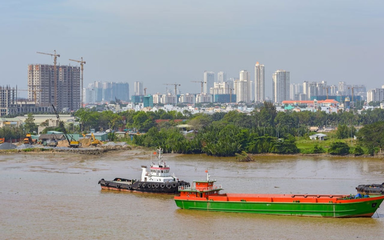 Ho Chi Minh City scene with river in foreground and various construction on high-rise buildings in background