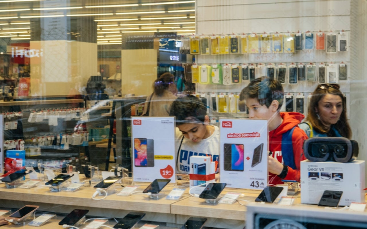 View from the street of young boys using electronics technology products inside modern supermarket tech store on main Baku avenue