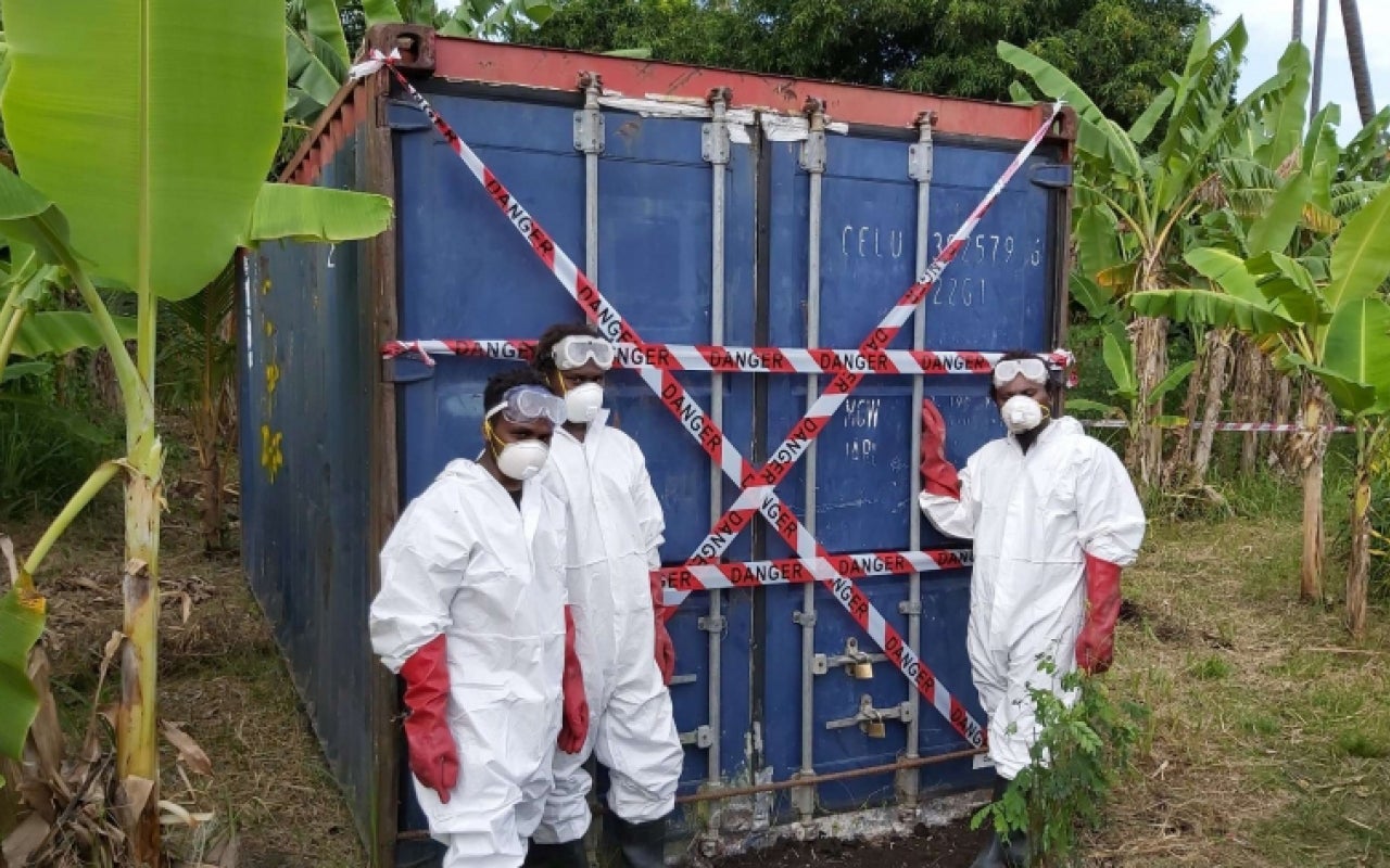 Men in HAZMAT suits in front of a shipping container full of DDT