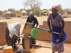 Women using a water pump in an arid landscape