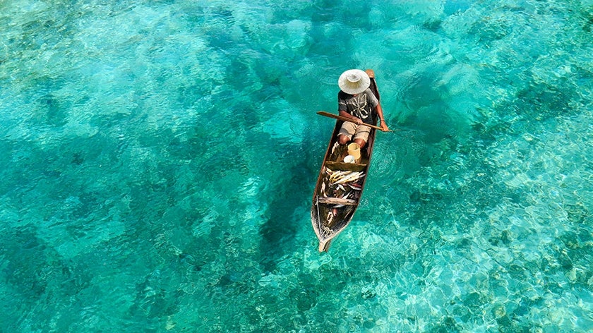 Fisherman in boat surrounded by clear, turquoise waters