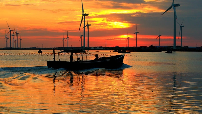 Boat traveling through an aquaculture area of the Yellow Sea. Windmills in background with colorful sunset