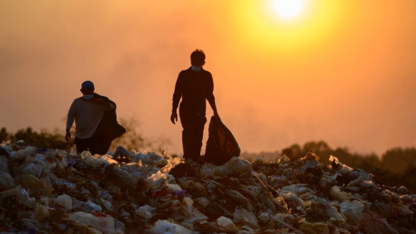 People at a landfill collecting trash with a bright sun in background