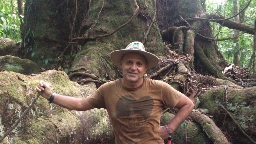 Man wearing a hat standing in front of a large tree