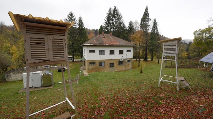 House in forested valley with two air quality monitoring stations in foreground
